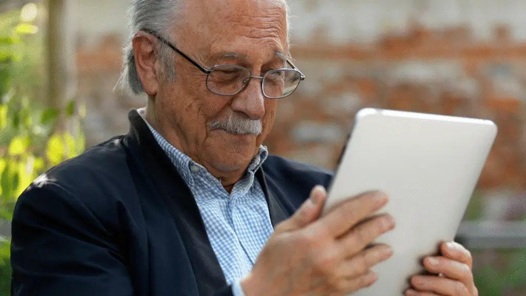 An older man who has graduated from the Community Clicks programme looking at his digital tablet smiling.