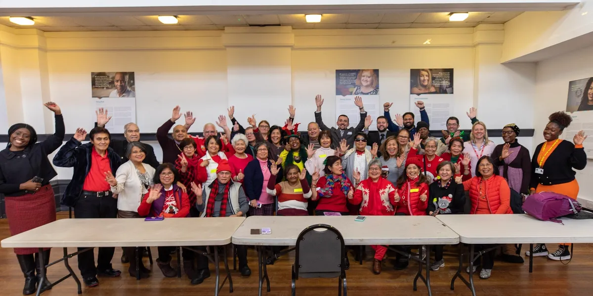 Lots of people with their hands in the air at a Community Clicks graduation, the front row is sitting and the back two rows are standing, everyone looks happy